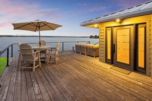 A wooden deck with a table and chairs, a large umbrella, and a building with glass doors.