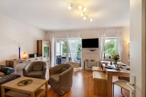 Un salon moderne comprenant un canapé, un fauteuil, une table à manger et un téléviseur fixé au mur.