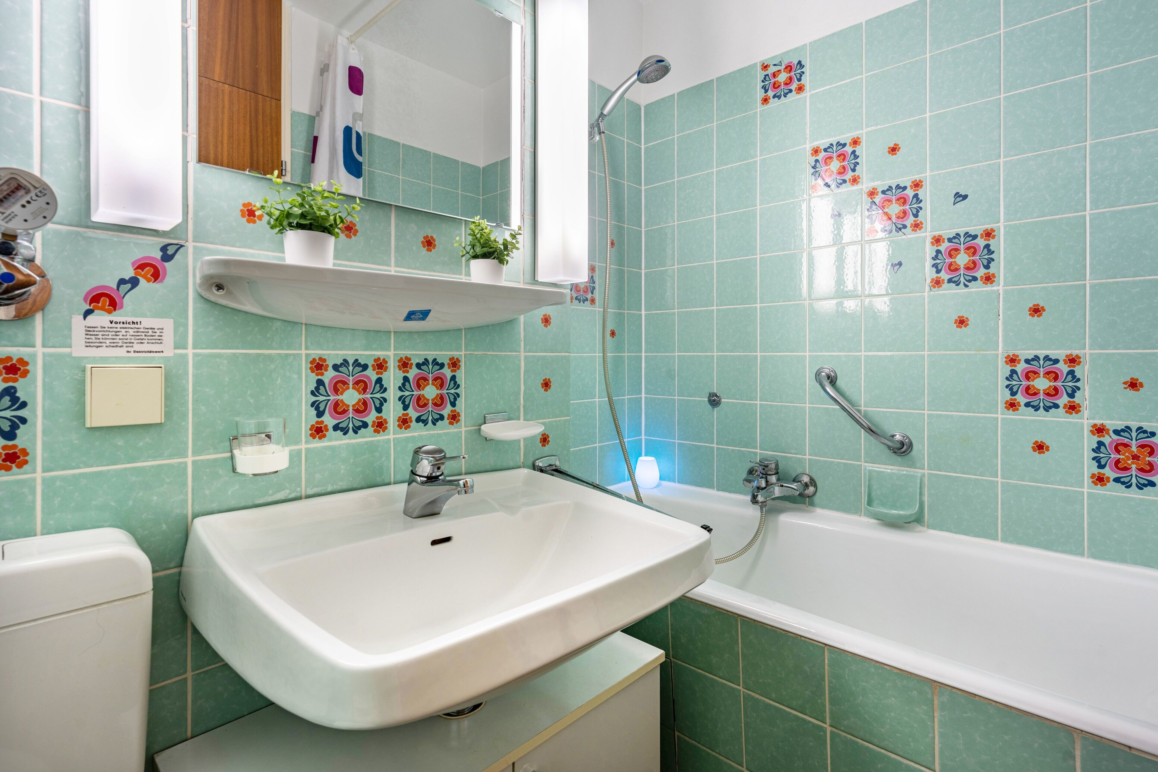 Een badkamer met een wastafel, spiegel, douche en decoratieve tegels.