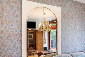 Quarto com um espelho grande, um candelabro, uma televisão e um sofá.
