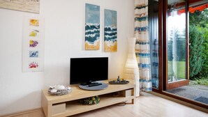 Un soggiorno moderno con televisore a schermo piatto, mobile TV in legno, opere d'arte e vista panoramica attraverso una porta in vetro.