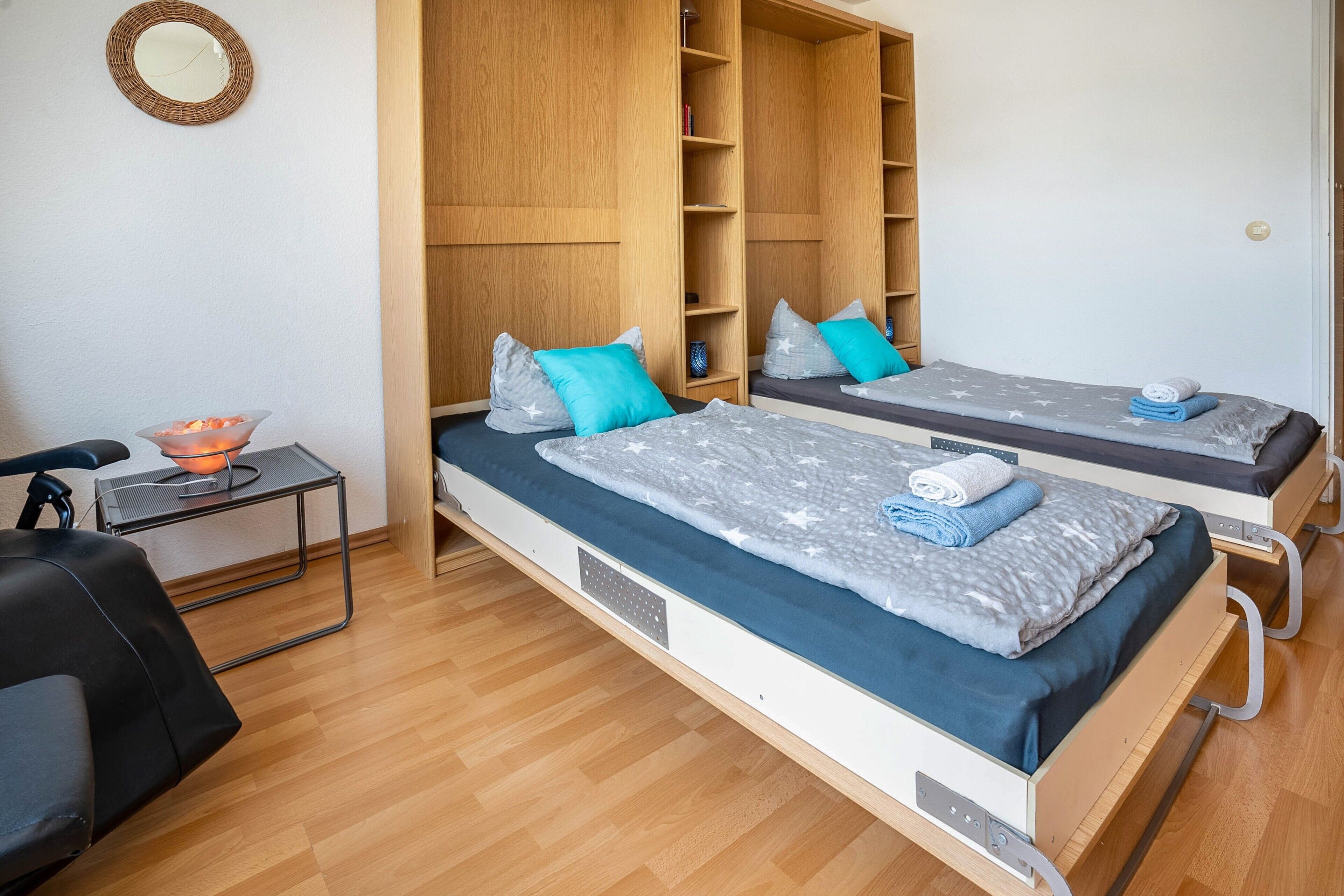 Ein Zimmer mit zwei Betten, einem kleinen Tisch mit einer Schale, einem Stuhl und einem Holzschrank.