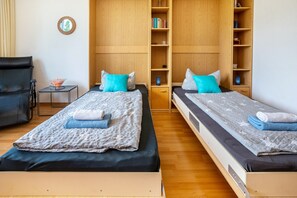 Une chambre avec deux lits, une petite table sur laquelle se trouve un bol, une chaise et des étagères en bois remplies de livres.