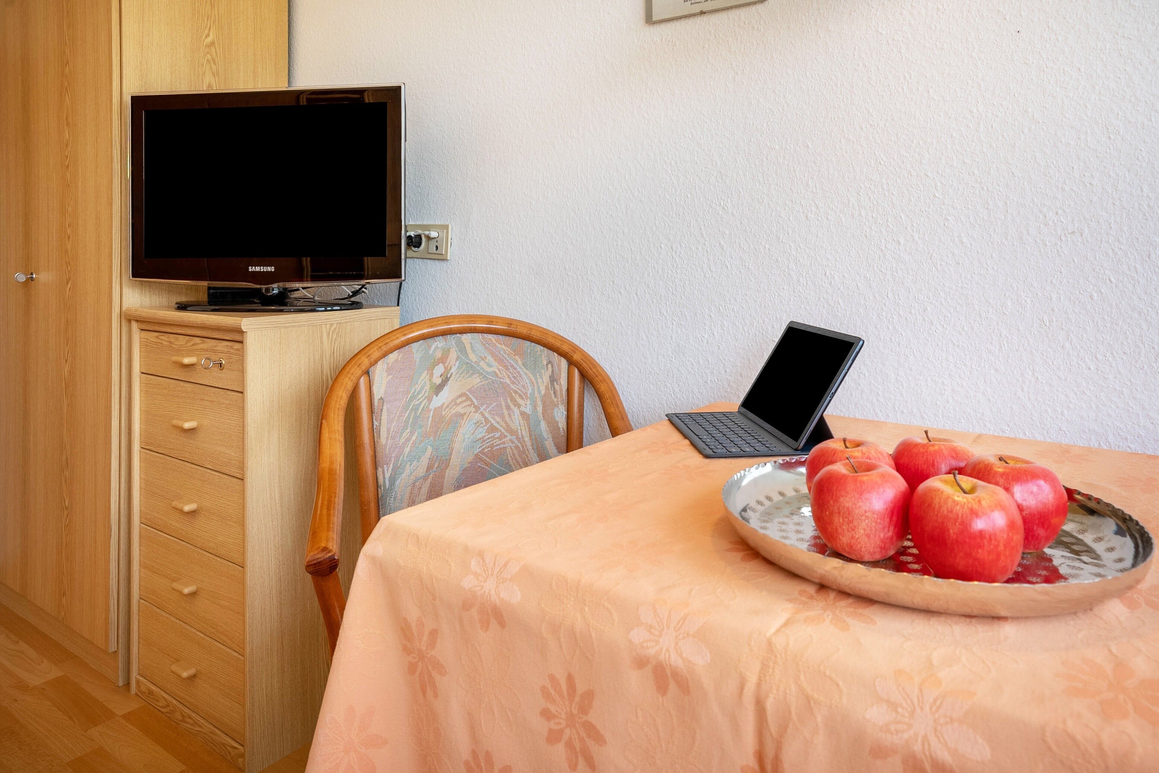 Een kamer met een houten kast, een televisie, een laptop op een tafel en een schaal met appels.