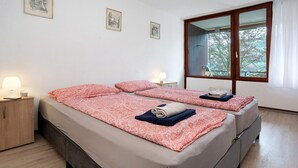 A double bed with a patterned bedspread, a bedside table with a lamp, and a window with a view of trees. - Apartment No. 19 with Shared Garden, Balcony and Wi-Fi (Bad Herrenalb)