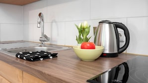 A kitchen with a sink, a kettle, a bowl with a red apple and green leaves, and a black and white polka-dotted cloth. - Apartment No. 19 with Shared Garden, Balcony and Wi-Fi (Bad Herrenalb)