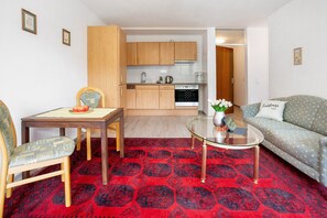 Una sala de estar con sofá, una mesa de centro de vidrio, una mesa de comedor con sillas, y una cocina al fondo.