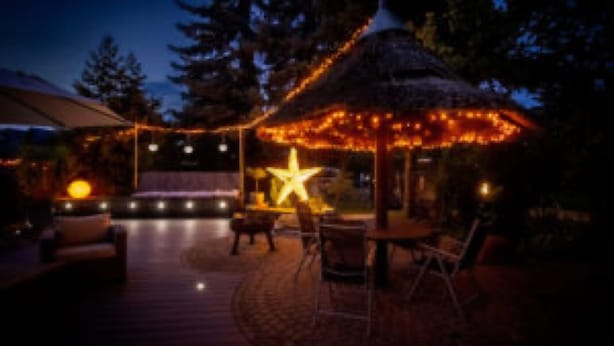 Ein Terrassenbereich im Freien mit einem Gazebo mit Reetdach, Lichterketten und einer Sterndekoration.