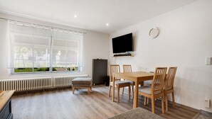 Ein modernes Zimmer mit Esstisch, Stühlen, einem an der Wand befestigten Fernseher und einem Fenster mit Vorhängen.