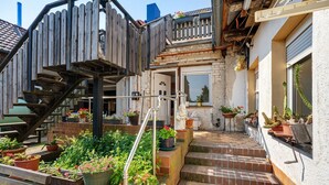 Ein Wohnhaus mit Holzterrasse, Sitzgelegenheiten im Freien und verschiedenen Kübelpflanzen.
