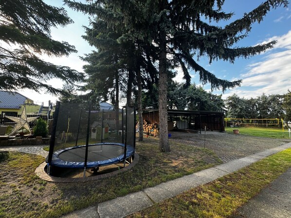 Un trampoline installé dans un espace verdoyant, avec des arbres et un bâtiment en arrière-plan.