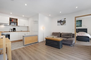 A compact living space with a kitchenette, a sofa, a bed, and a floor lamp.
