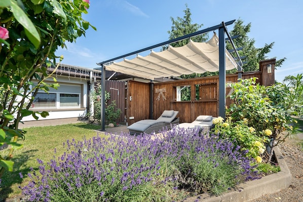 A patio with a pergola, outdoor seating, and a garden with lavender and yellow flowers.