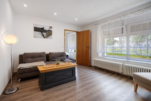 Uma sala de estar moderna com sofá, mesa de centro, luminária de chão, radiador e janela com vista.