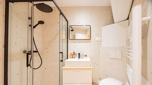 Un baño moderno con ducha envuelta en vidrio, lavamanos blanco con artículos de aseo y un inodoro.