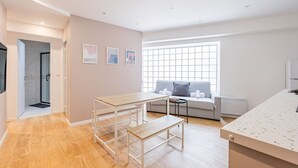 Un apartamento moderno con suelo de madera, un sofá gris con cojines, una mesita y una ventana con persianas.