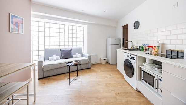 Una cocina moderna con lavadora integrada, una zona de comedor con mesa y sofá, y un ventanal que proporciona luz natural.