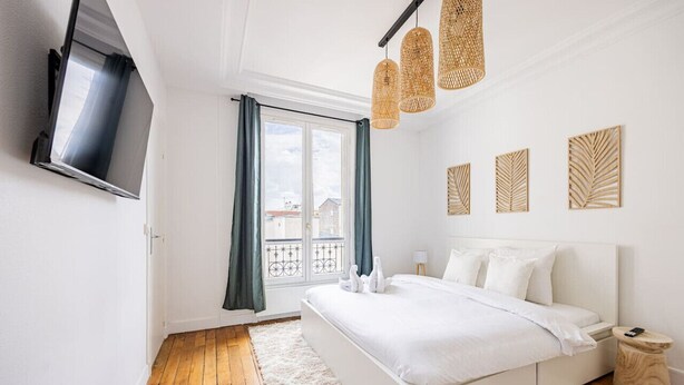 Un dormitorio con una cama grande, un televisor en la pared y un balcón con cortinas.