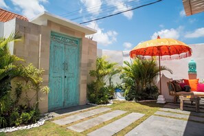 Un patio con una puerta turquesa, un paraguas rojo y amarillo, y una estatua de Buda.