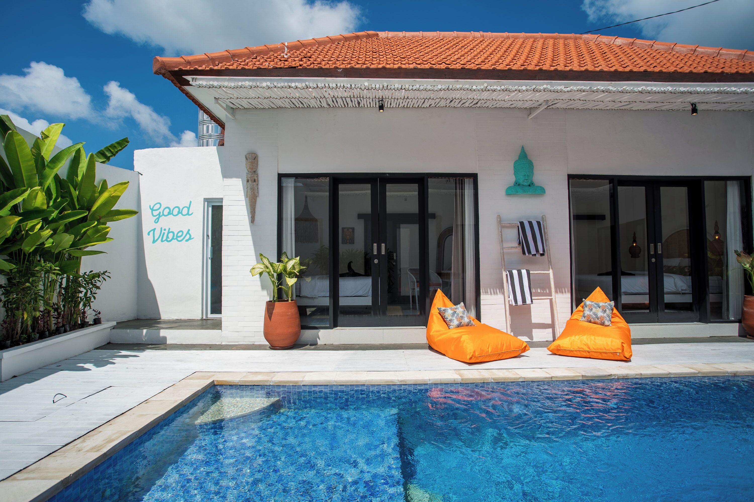 Ein modernes Gebäude mit Schwimmbecken, zwei orangefarbenen Sitzsäcken und einem Schild mit der Aufschrift 'Good Vibes'.