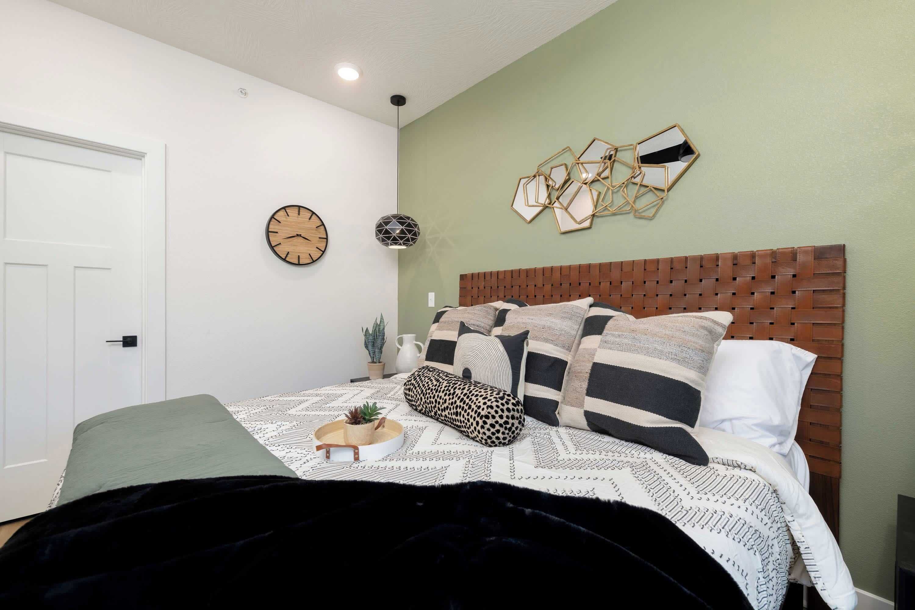 Ein Schlafzimmer mit einem Holz-Kopfteil, einem Bett mit gemusterten Betttextilien, einer Wanduhr und einer geometrischen Wanddekoration.