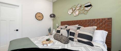 Una camera da letto con una testiera in legno, un letto con biancheria a motivi e una decorazione geometrica a parete, oltre a una sveglia da parete.