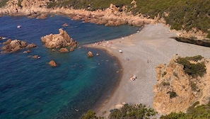 A coastal landscape with rocky formations, clear blue waters, and a sandy beach.