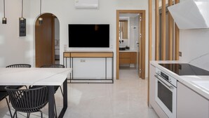 Una cocina moderna con horno integrado, un comedor con mesa y sillas, y un televisor de pantalla plana montado en la pared.