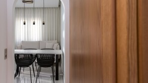 Un comedor moderno con una mesa blanca, sillas negras y un sofá blanco bajo un ventanal con cortinas.
