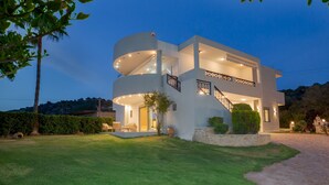 A modern two-story house with a circular central section, a staircase, and a well-maintained lawn. - Adore Gold Natural Retreat by Estia (Mylopotamos)