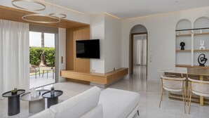 A modern living room with a sofa, coffee table, TV, and dining area. - Adore Gold Natural Retreat by Estia (Mylopotamos)