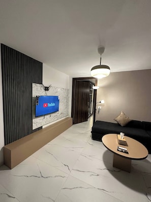 A modern living room with a flat-screen TV mounted on a marble wall, a sofa, a coffee table, and a door leading to another room.