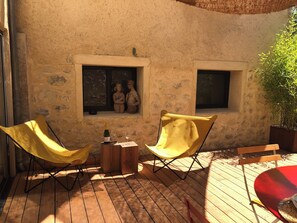 A wooden deck with two yellow chairs, a small table with a bottle and glasses, and a red table.