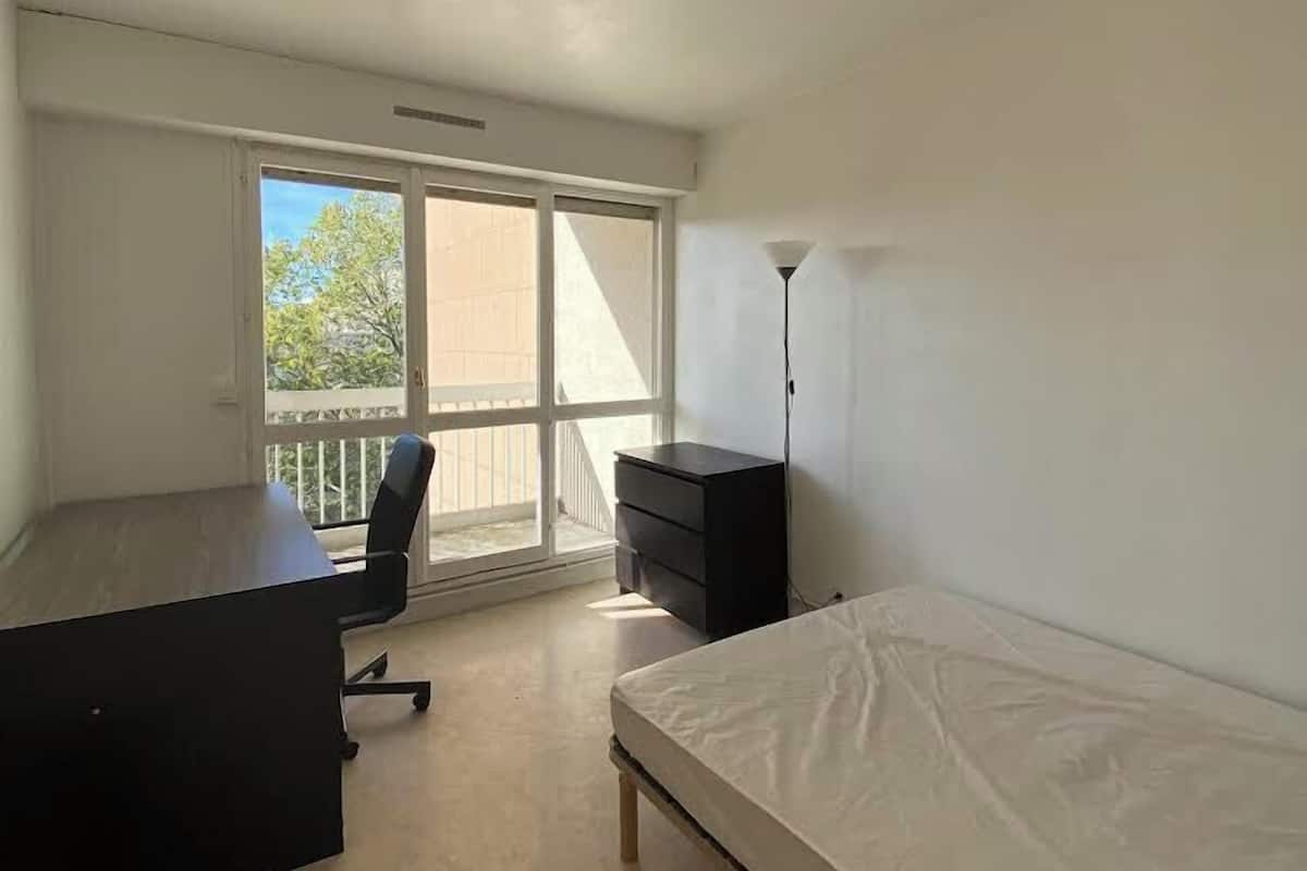 A room with a bed, a desk, a chair, a dresser, and a window with a view of trees.