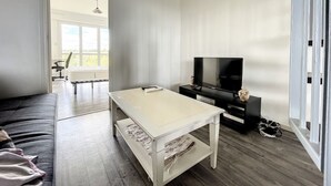 Un soggiorno moderno con un divano, un tavolino, una TV su un mobile e vista sull'esterno attraverso un'ampia finestra.