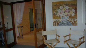 A room with two wooden director chairs, a painting of flowers on the wall, and a partially open door leading to another room.