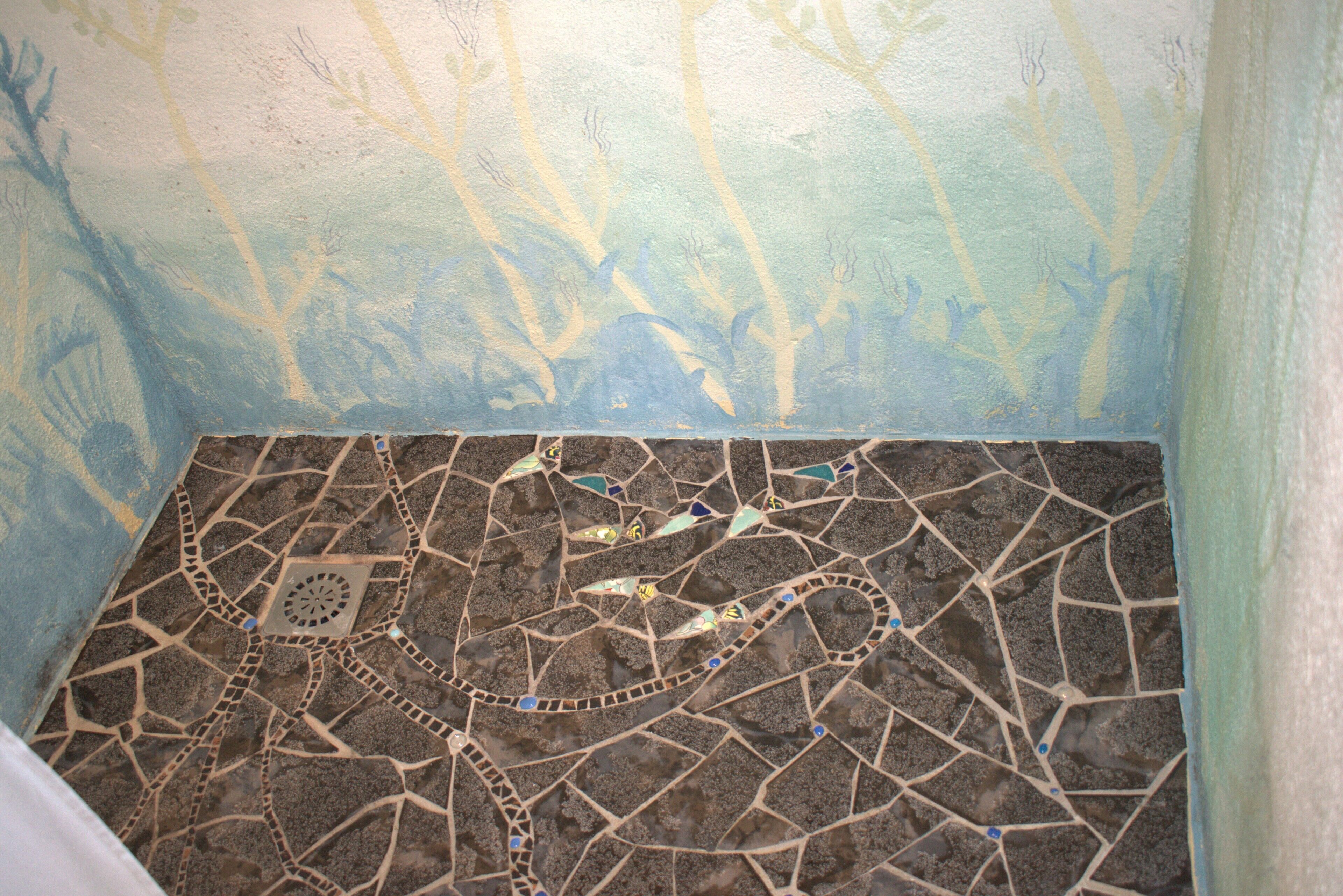 A mosaic floor with a geometric pattern and a painted wall with tree-like designs.
