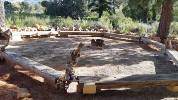 Un'area esterna rustica con un recinto circolare in legno, tronchi e rocce.