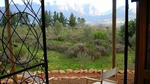 A view from a room with a wooden door, through a metal gate, overlooking a landscape with mountains and greenery.