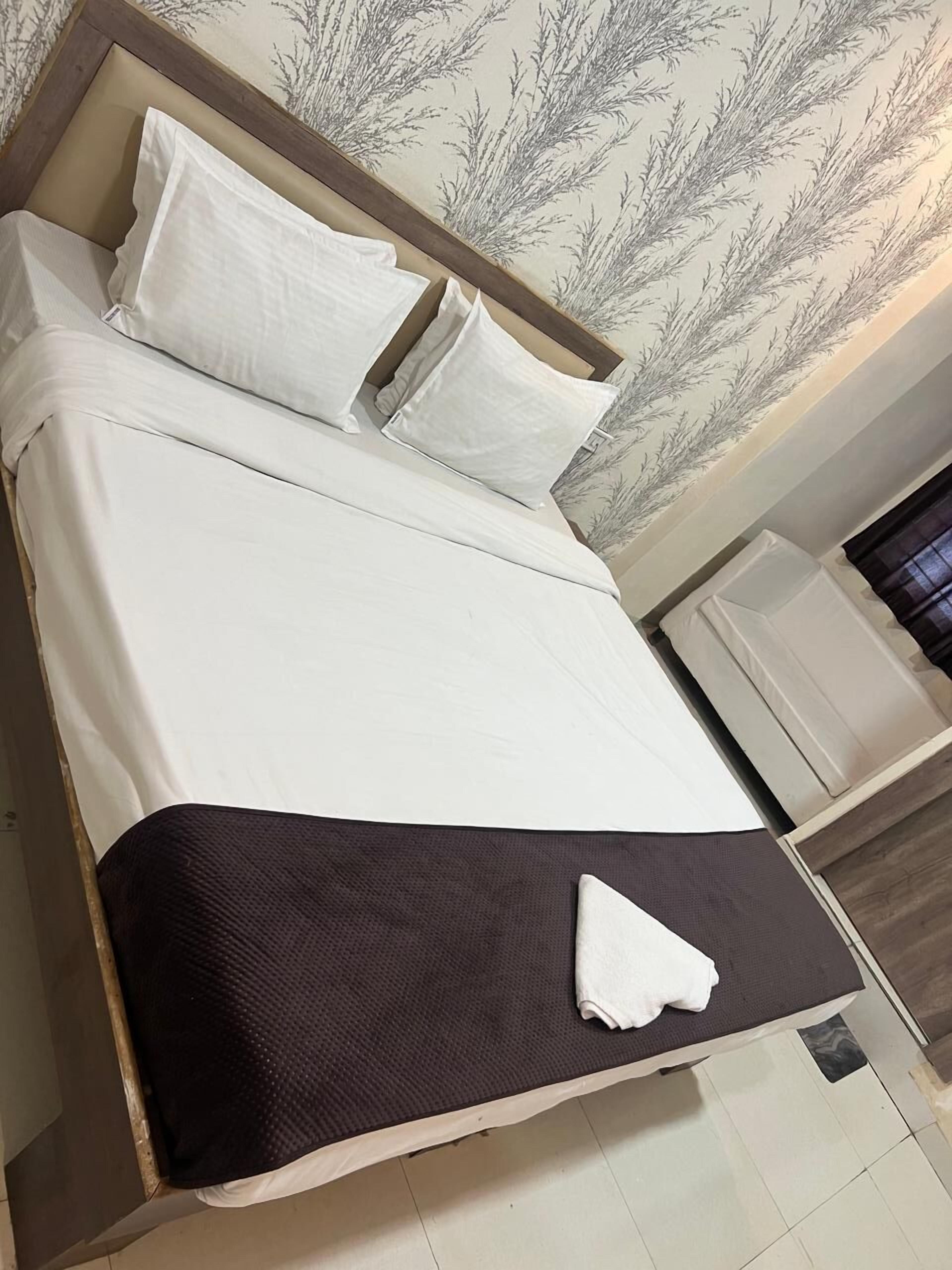 A neatly made bed with white bedding and a brown throw blanket.