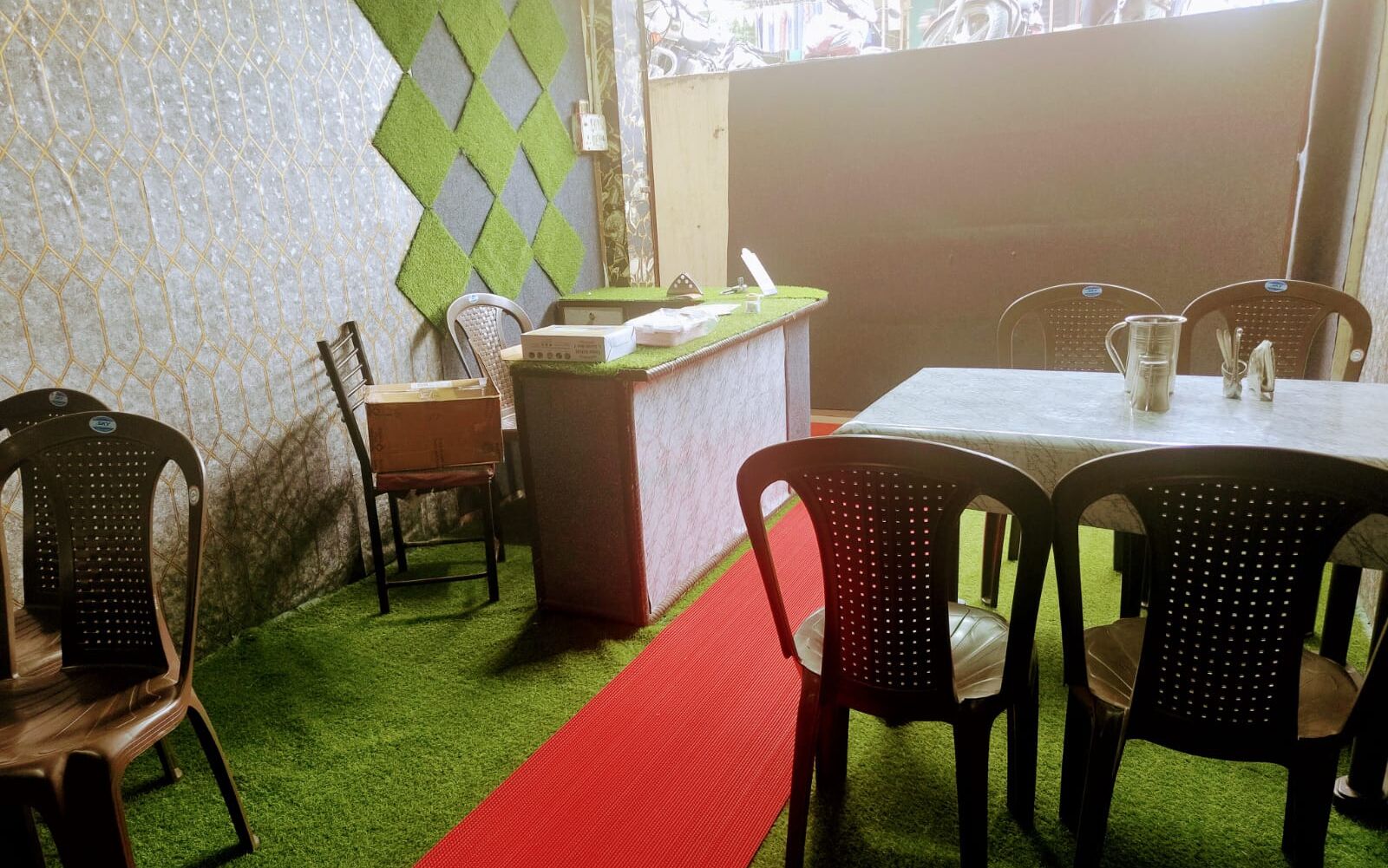 A restaurant interior with a red carpet, green artificial grass, and a counter with chairs around it.