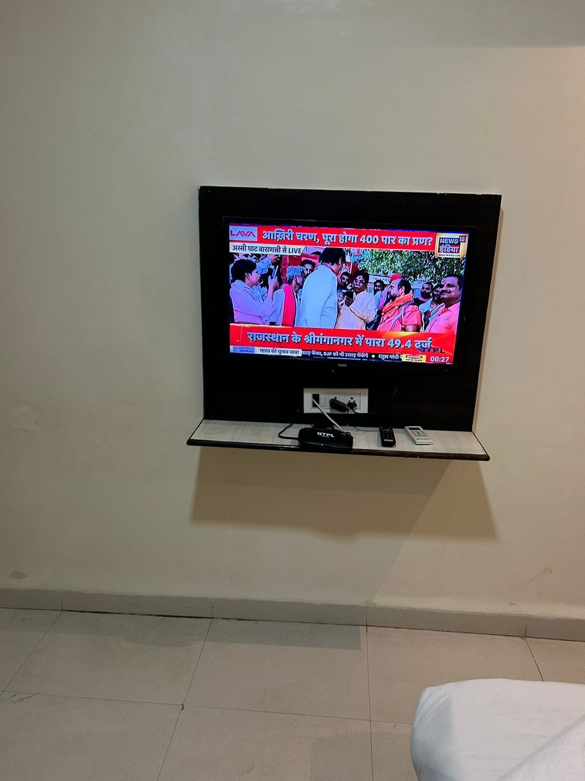 A flat-screen TV mounted on a wall, displaying a news channel with Hindi text.