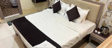 A neatly made bed with white and black bedding, a wooden nightstand with a tray containing a kettle and cups, and a bathroom visible through an open door.