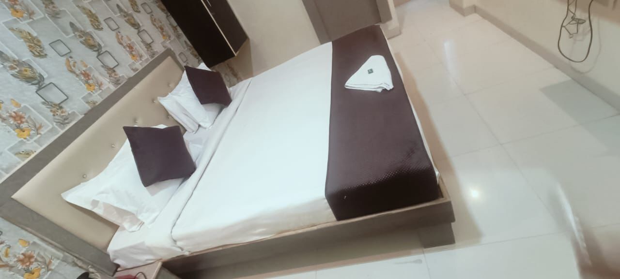 Een net opgemaakt bed met witte en donkere kussens, een zwart hoofdbord en een witte nachtkastje met een opgevouwen witte doek.