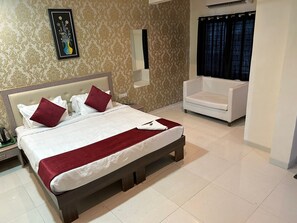 A hotel room with a large bed, a white armchair, a mirror, and a framed artwork on the wall. - Hotel SS-1 (Indore)