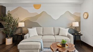 A modern living room with a sofa, two side tables, a coffee table, and a wall mural. - Beautiful New Downtown Columbia Falls Condo near Glacier National Park! (Columbia Falls)