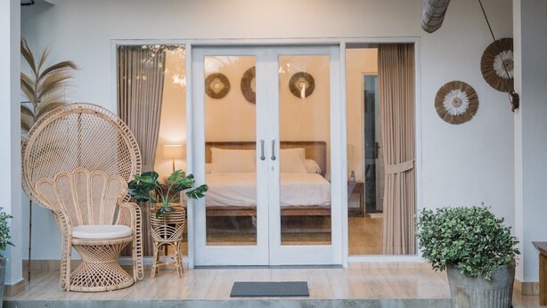 A room with a bed, a wicker chair, a potted plant, and a glass door leading to another room. - Villa Leya Canggu - Ella Villa Bali (Canggu)