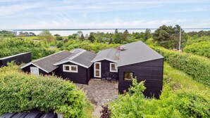 A black wooden cabin with a sloped roof, a small porch, and a view of a lake. - "Skamhals" - 440m to the fjord by Interhome (Frederiksværk)