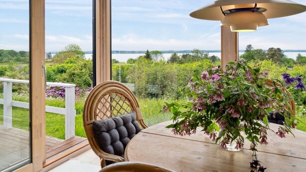 A wooden deck with a table and chairs, a hanging light fixture, and a view of a lake and greenery. - "Skamhals" - 440m to the fjord by Interhome (Frederiksværk)