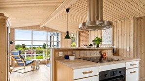 A modern kitchen with wooden cabinetry, a built-in oven, and a large window overlooking a garden. - "Skamhals" - 440m to the fjord by Interhome (Frederiksværk)
